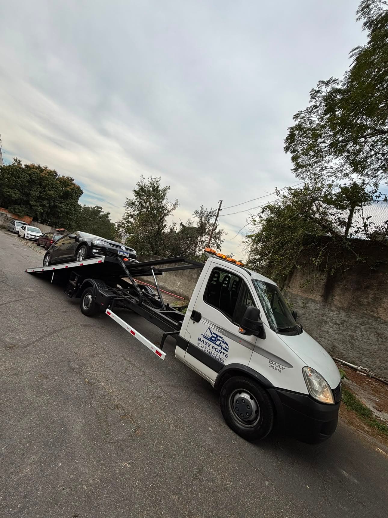 Guincho da Base Forte Guinchos com um carro preto sobre a plataforma, em uma rua de São Paulo